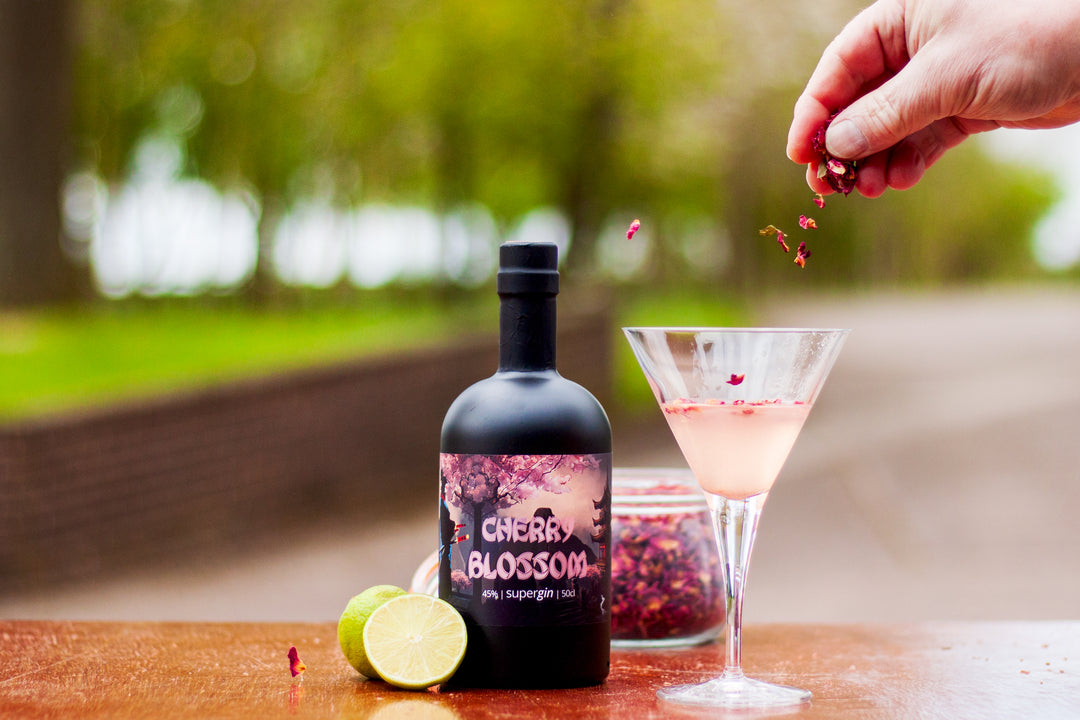 Roy Wood's Cherry Blossom Supergin with The Cherry Blossom cocktail. Hand sprinkling dried petals to garnish, set outside with blurred landscape.